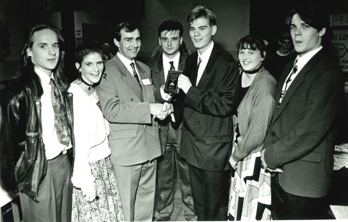 Members in suits and dresses at a presentation, one holding a plaque