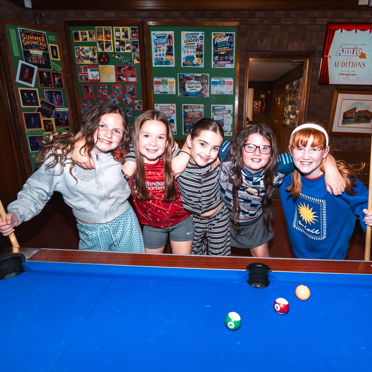 Young members smiling together at the pool table at a PYC club night